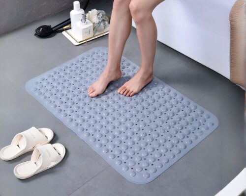 Femme posant ses pieds sur un tapis de bain gris. On voit seulement le bas de ses jambes.