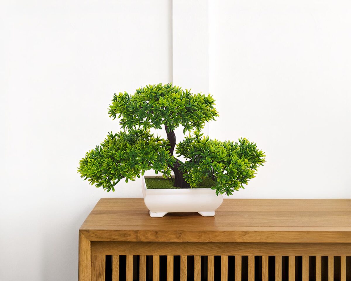 Bonsaï artificiel dans un pot blanc placé sur une étagère.