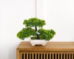Bonsaï artificiel dans un pot blanc placé sur une étagère.