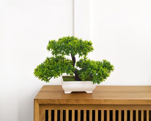 Bonsaï artificiel dans un pot blanc placé sur une étagère.