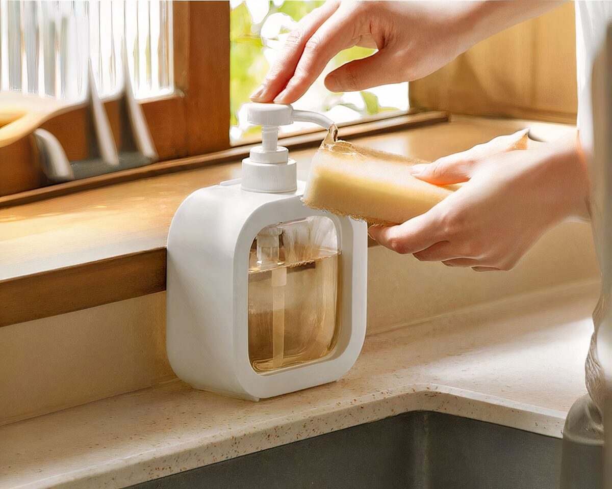 Distributeur de savon minimaliste blanc On voit une personne qui se sert d'un distributeur de savon blanc et transparent.