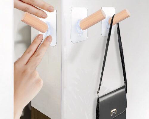 Trois patères autocollantes accrochées au mur avec un sac suspendu.