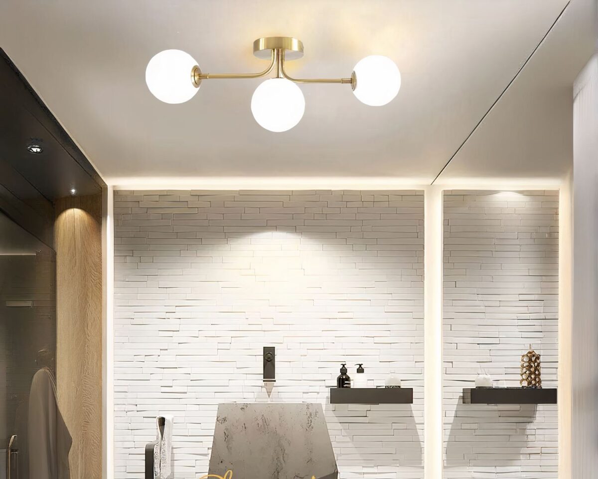 Photo d'un lustre salle de doré à 3 boules en acrylique dans une salle de bain blanche à parements en pierre