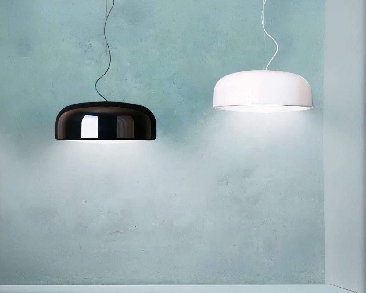 Photo d'un lustre blanc et d'un lustre noir minimalistes éclairés suspendus en deux longueurs devant un mur peint en bleu-vert