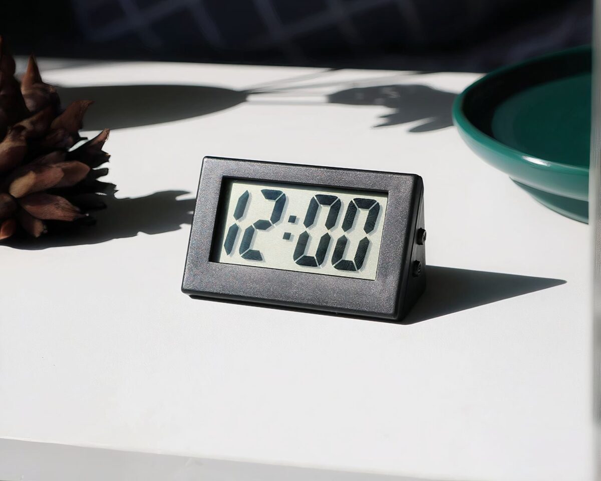 Petite horloge grise posée sur un support blanc.