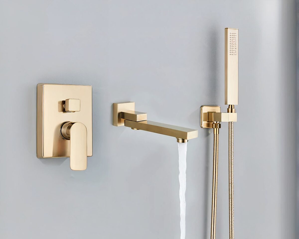 Photo d'un mitigeur salle de bain doré en trois parties avec l'eau qui coule du bec pivotant, le mitigeur à gauche et la doucette à droite le tout sur un mur gris