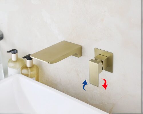 Photo d'un mitigeur mural doré brosse contemporain avec bec cascade au dessus d'un lavabo blanc sur un mur beige