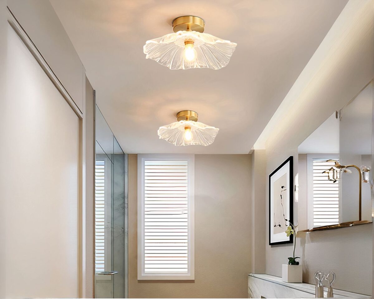 Photo de deux plafonniers en verre froissé sur le plafond d'une salle de bain aux murs clairs, une porte vitrée à gauche et le robinet du lavabo en marbre en bas