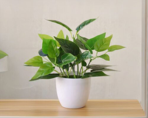 Plante artificielle dans un pot blanc posé sur une table.