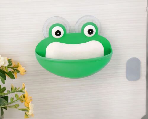On voit un porte-savon en forme de grenouille pour enfant. Ile st accroché au mur avec une ventouse.